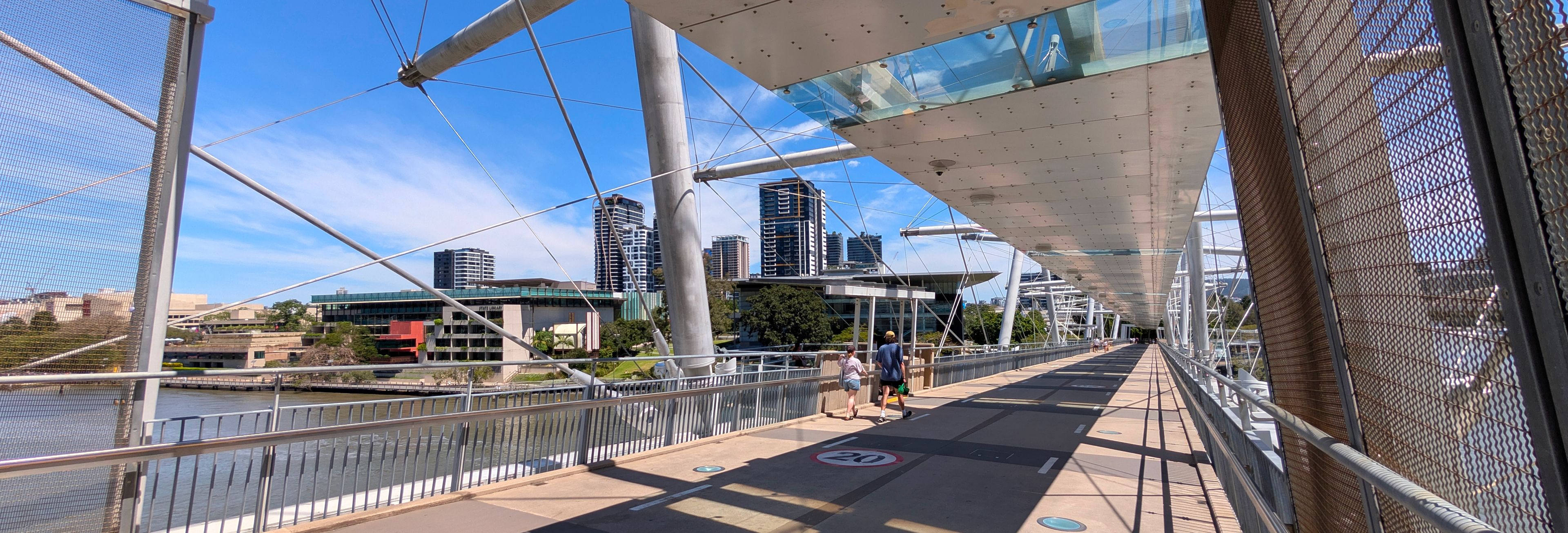 Kurilpa Bridge at night, the cantilevers lit in red. GOMA is illuminated blue in the background. The footpath is brightly lit in warm light.