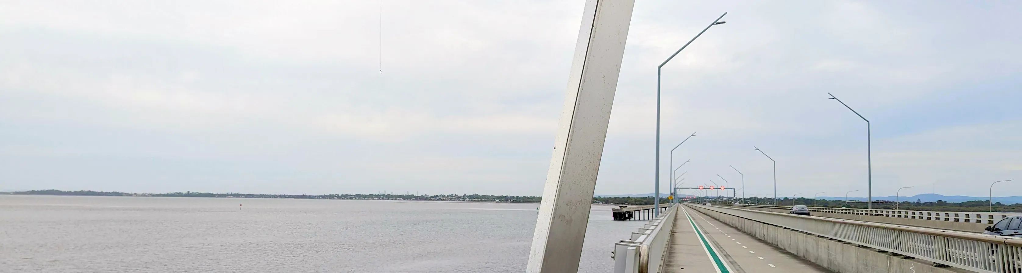 A featureless concrete bridge spanning over a vast bay, a green painted bike lane disappearing into the distance