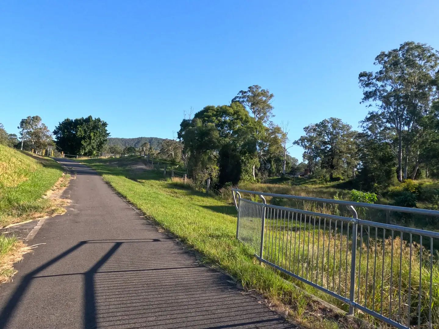 A bike path with a small bridge weaves through a grassy rural area
