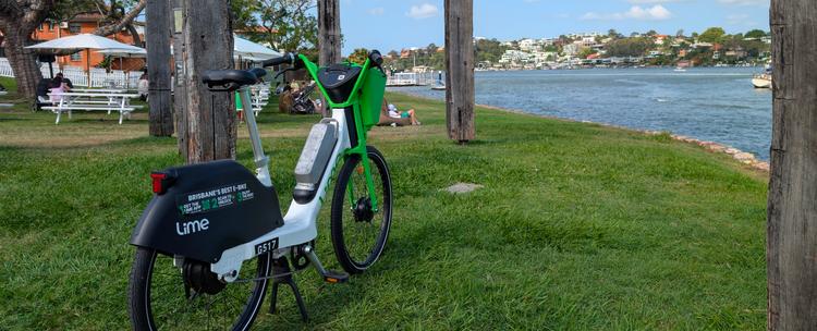 A green Lime bike sits next to the Brisbane River