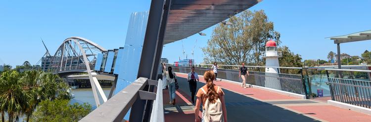 Looking along the Goodwill Bridge on a sunny day as people walk by, QUT, the Captain Cook Bridge and Kangaroo Point in the background.