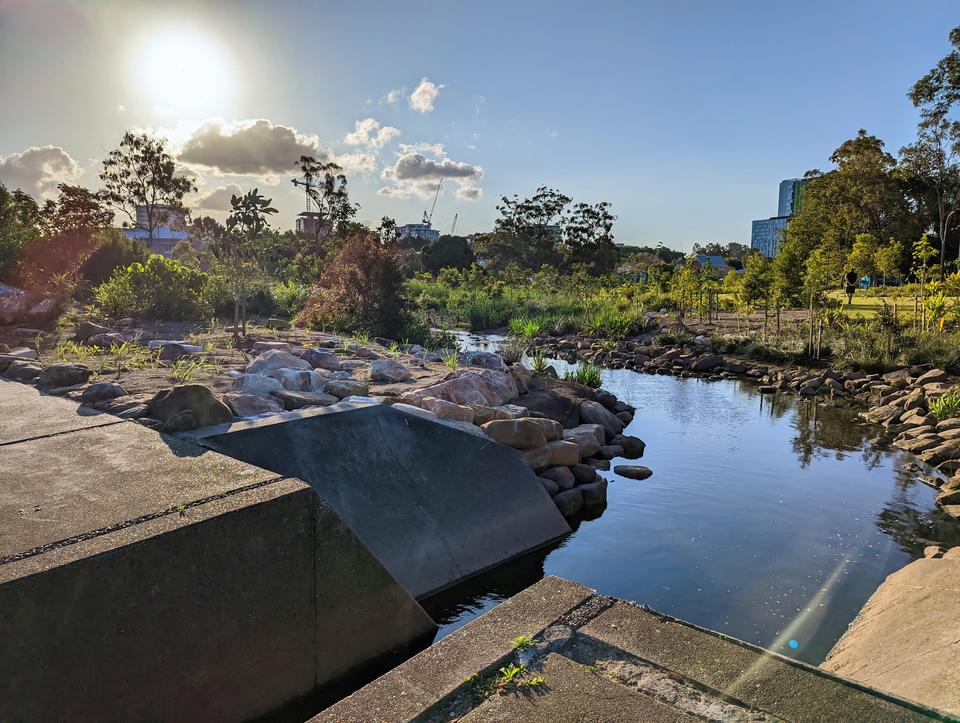 A concrete drain empties into a freshly planted creek system, with rocks, vegetation and grasslands