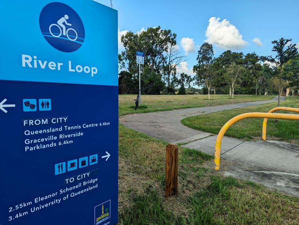A Riverloop sign shows directions to and from the city, next to an off-road bikeway
