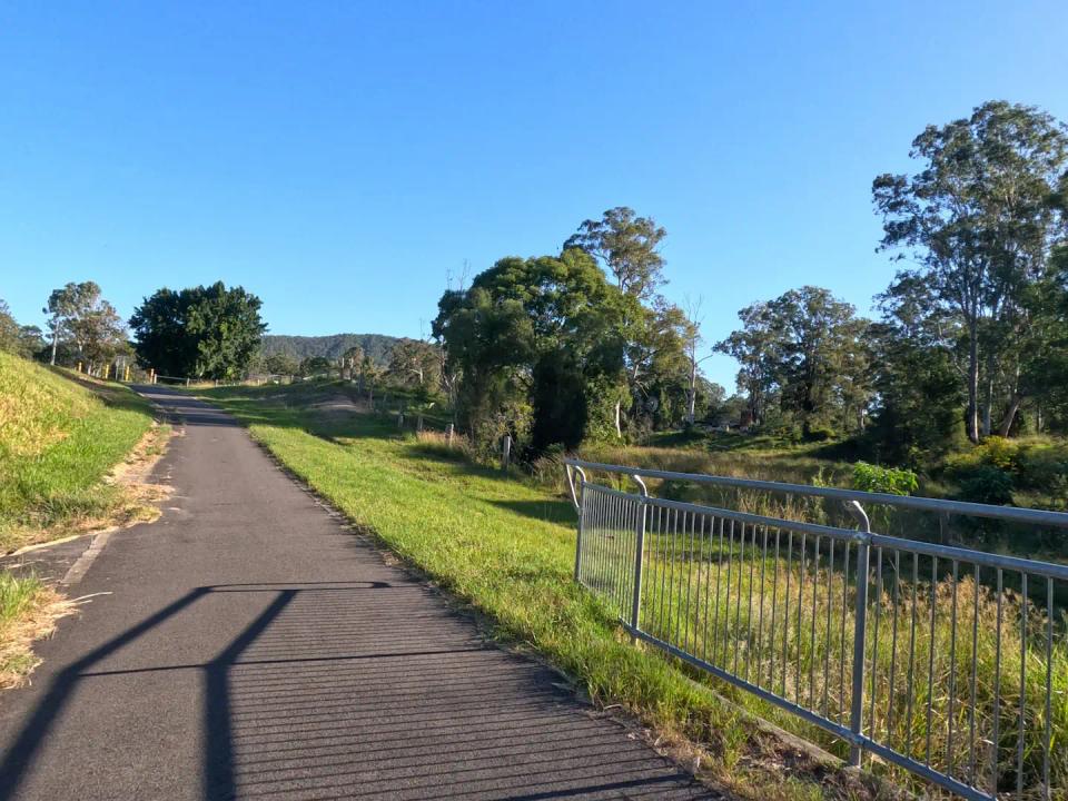 A bike path with a small bridge weaves through a grassy rural area