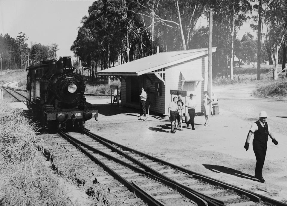 A steam train pulls up to a small wooden building at Wamuran station in 1967